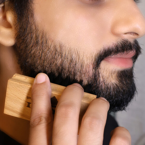 A man holds a beard brush in his well-groomed beard, highlighting its neat and tidy appearance.