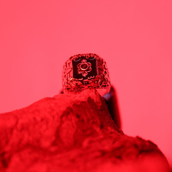 A black Zenith ring placed on natural wood, featuring a front view with red lighting.