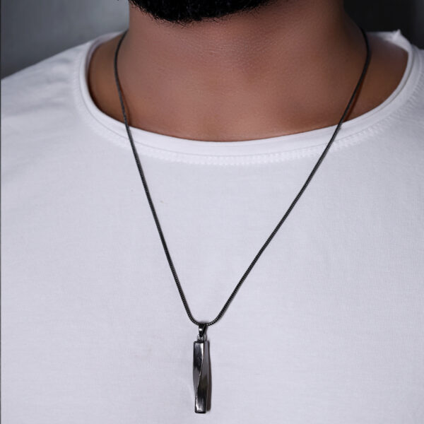 "Man wearing a twisted bar pendant on a thin chain, visible against a white T-shirt. The pendant is centered on the chest area of the shirt."