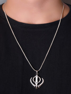 "Man wearing a Khanda pendant on a chain, visible against a black T-shirt. The pendant, featuring the Khanda symbol, stands out prominently against the dark background, emphasizing its detailed design."