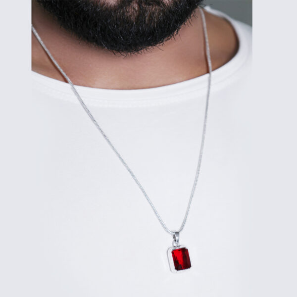 "Man wearing a red stone pendant on a chain, visible against a white T-shirt. The vibrant red stone stands out against the white shirt, drawing attention to the pendant's bold color and design."