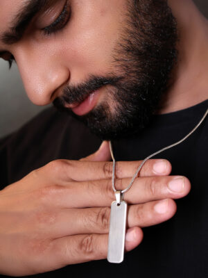 "Man wearing a silver bar pendant on a chain, visible against a black T-shirt. He is holding the pendant with his hand and looking at it, with the focus on the pendant and the contrast between the silver and the black shirt."