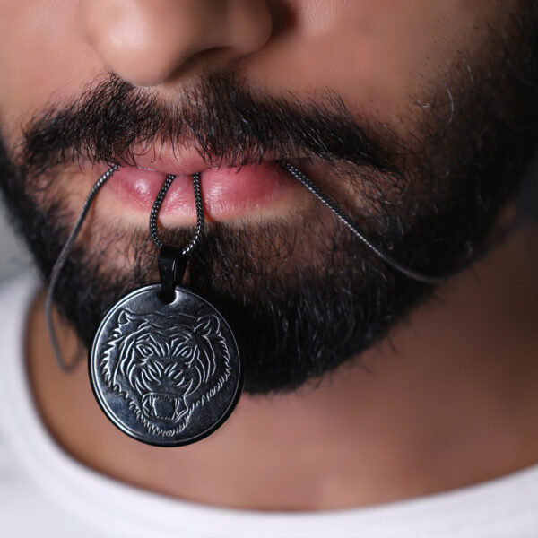 "Man holding a lion face pendant chain with his lips. The pendant is positioned near his mouth, with the chain draped in front of his face, and the focus is on the pendant's design."