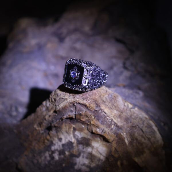 A black ring with a blue stone in the center, resting on dark wooden background.