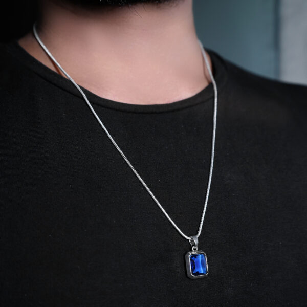 "Man wearing a blue stone pendant on a chain, visible against a black T-shirt. The vibrant blue stone stands out prominently, contrasting with the dark shirt and highlighting the pendant's striking design."