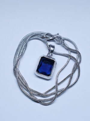 "Blue stone pendant with a chain, displayed against a white background. The vivid blue of the stone stands out, contrasting sharply with the clean, white backdrop and drawing attention to the pendant's elegant design."