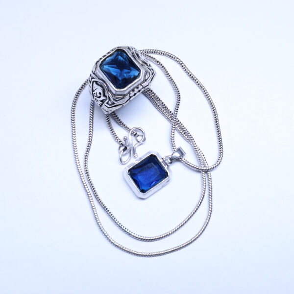 A close-up shot of a ring and pendant with large blue gemstones, both featuring a silver-colored finish, displayed against a white background.